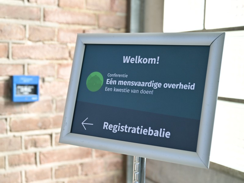 Wegwijzerpaal met printje met Welkomstbericht en een pijl naar de registratiebalie