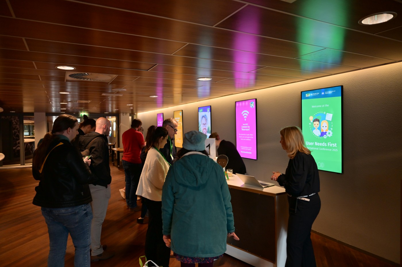 Gasten van de User Needs First Conference bij de ingang met schermen op de achtergrond